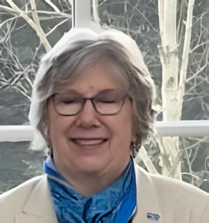 Smiling woman wearing glasses and a blue scarf with her back to a window